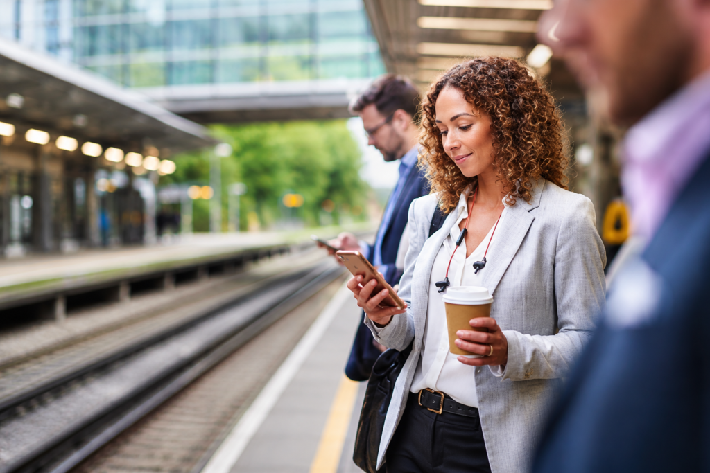 Professionnelle consultant son smartphone sur un quai de gare moderne dans un contexte de mobilité et de finance digitale